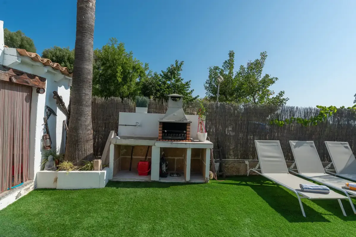 Un patio exterior tiene una parrilla, césped artificial y tumbonas reclinables.