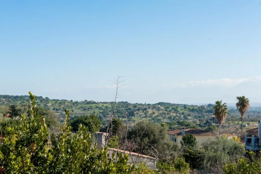 Un paisaje rural con colinas verdes, casas dispersas y árboles bajo un cielo despejado.