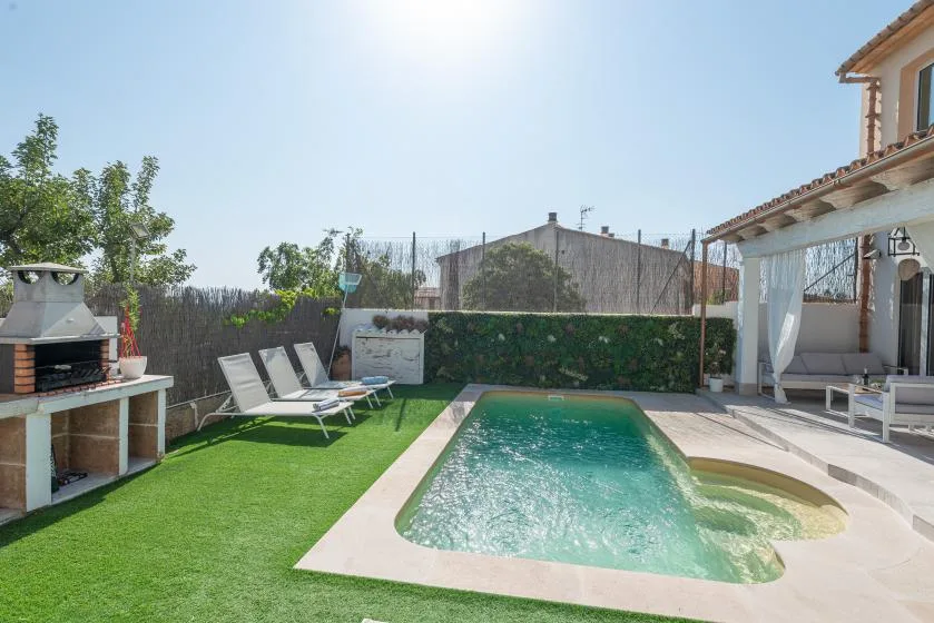 Zona de piscina exterior con una piscina pequeña, asientos y una barbacoa empotrada.