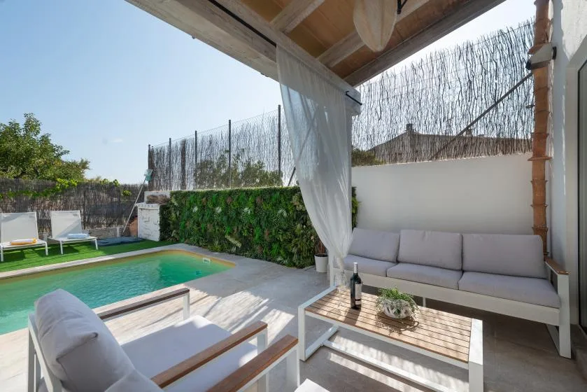 Una zona de estar exterior cubierta da a una piscina y un jardín.