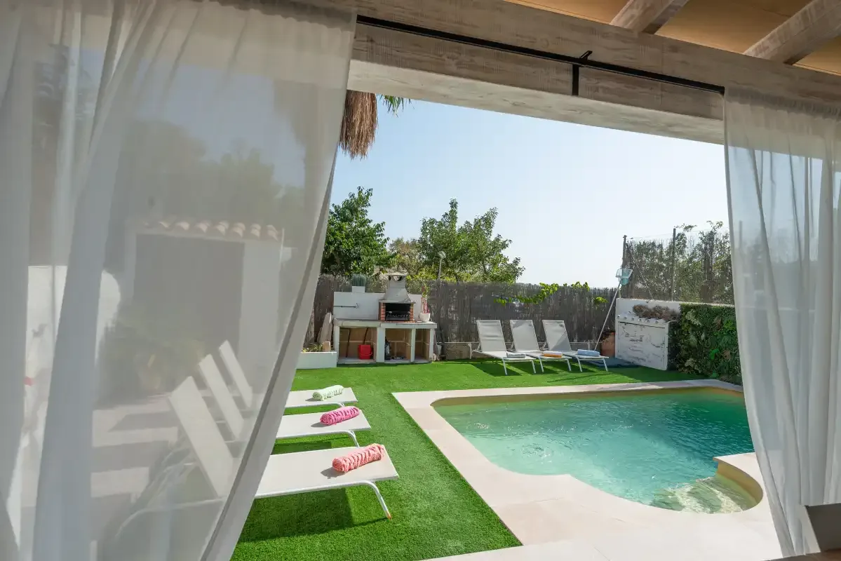 Una piscina y tumbonas están en una terraza verde bajo un patio cubierto.