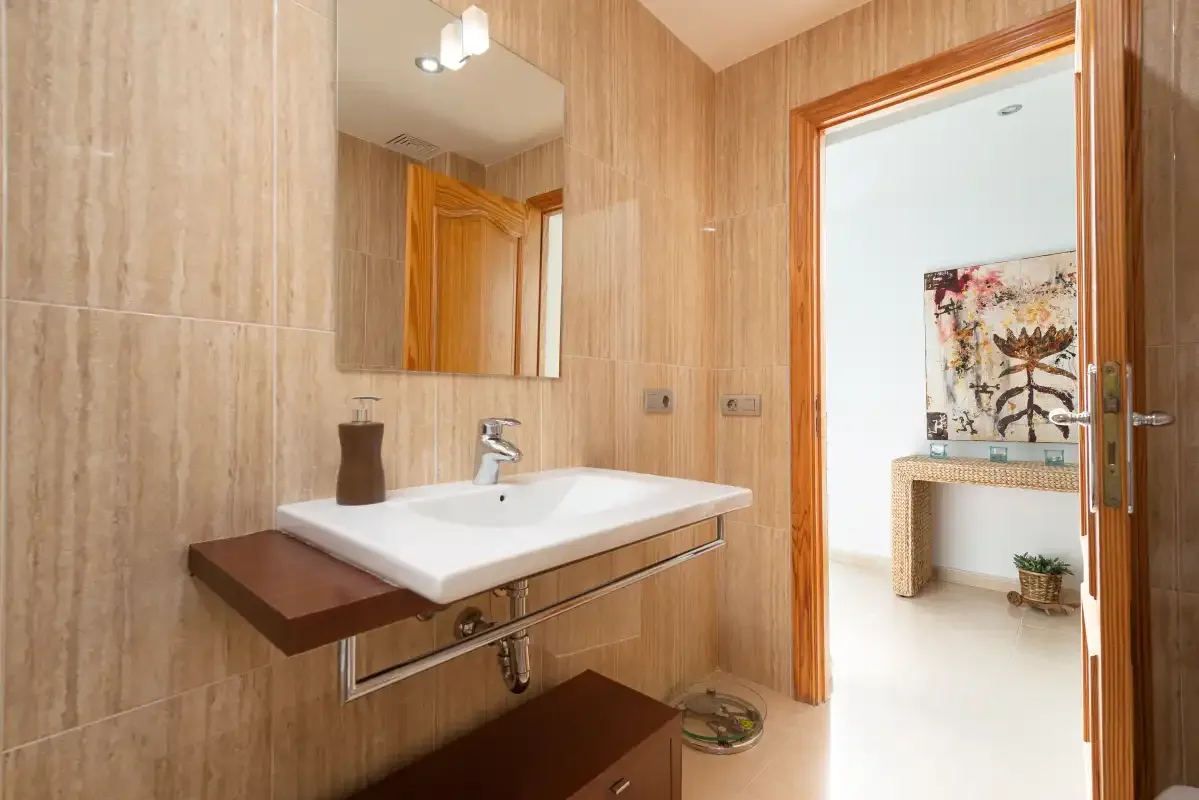 Un lavabo de baño con espejo está junto a una puerta de madera abierta.