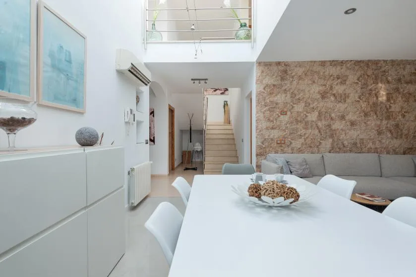 Un comedor luminoso con una larga mesa blanca junto a un sofá gris.