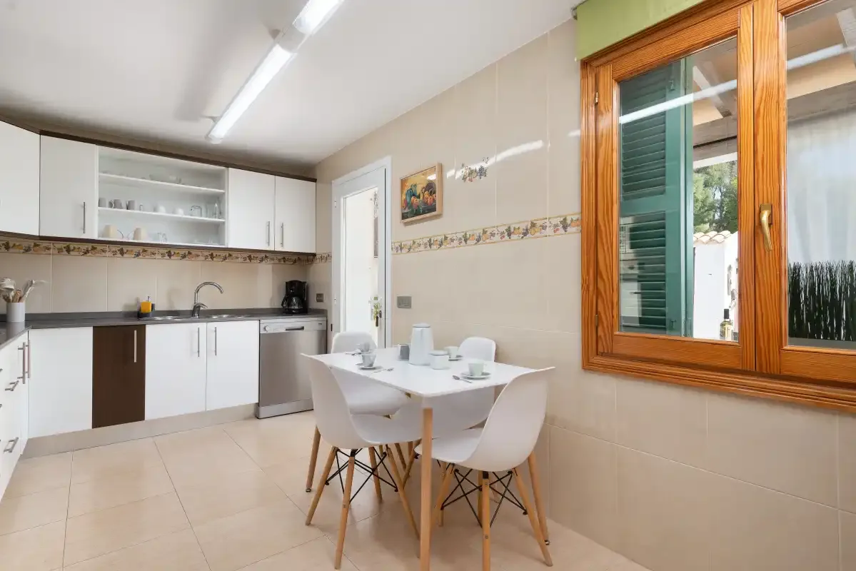 Una cocina y comedor con armarios blancos y una mesa junto a la ventana.