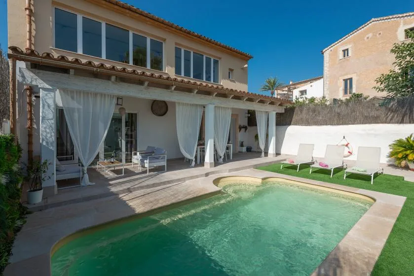 Una piscina junto a una casa con un patio cubierto y asientos al aire libre.