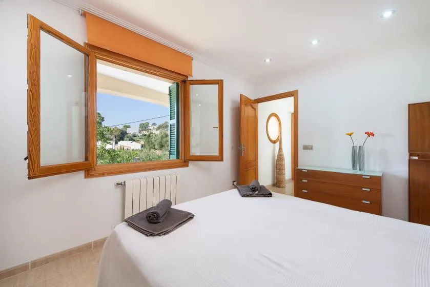 Un dormitorio luminoso con una ventana grande abierta y una cama bien tendida.