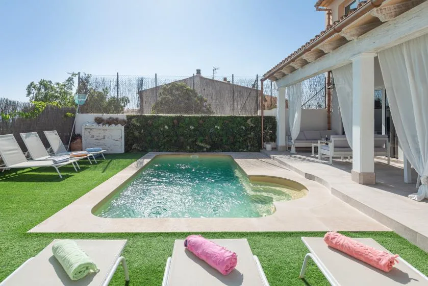 Una piscina exterior está junto a un patio cubierto, con tumbonas sobre el césped.