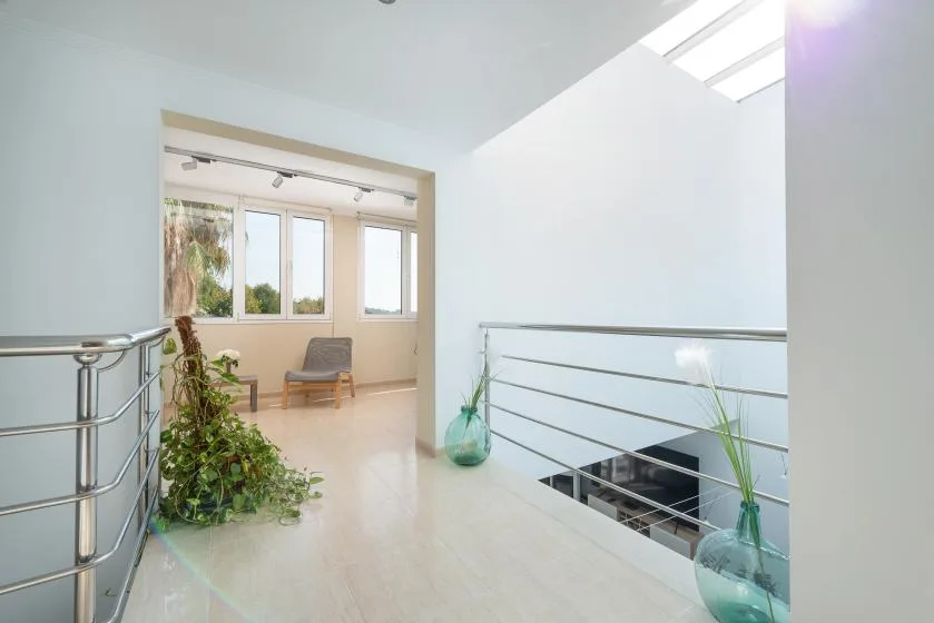Un descansillo luminoso da a una zona de estar soleada con ventanas y plantas.