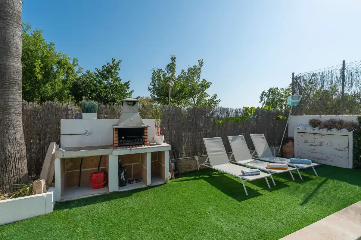Un patio exterior tiene una barbacoa empotrada, césped artificial y tumbonas reclinables.