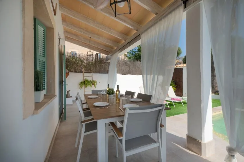 Comedor exterior cubierto con una mesa de madera y sillas junto a cortinas translúcidas.