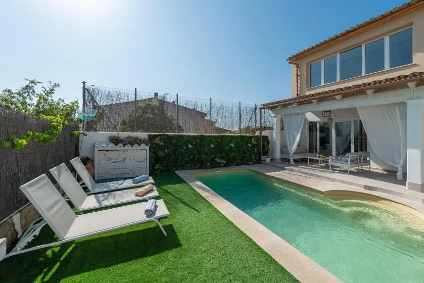 Una piscina en el patio junto a una terraza con asientos al aire libre y césped artificial.