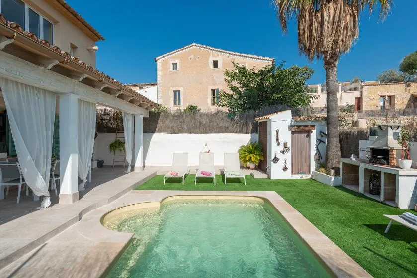 Un patio ajardinado con piscina, césped y una zona de estar a la sombra.