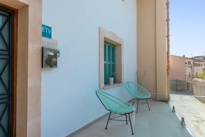 Una pequeña terraza tiene dos asientos turquesa junto a una ventana.