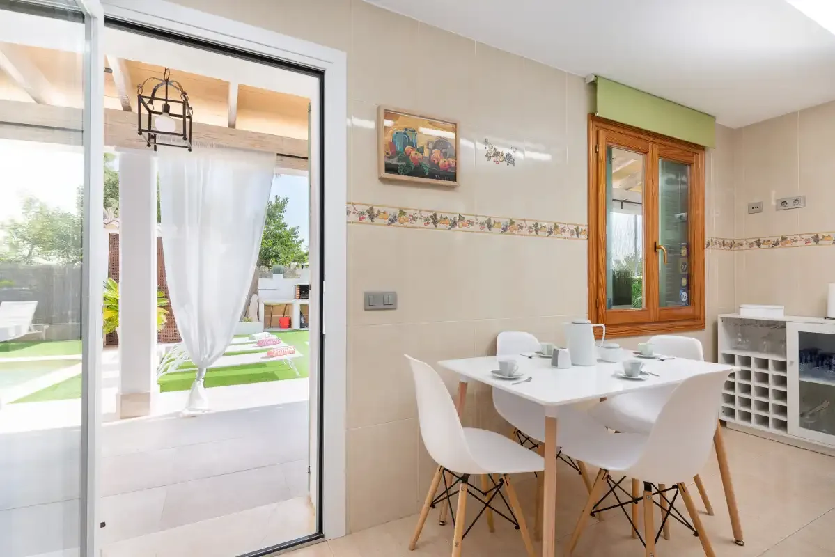 Un comedor luminoso con una mesa blanca junto a una puerta de cristal al patio.