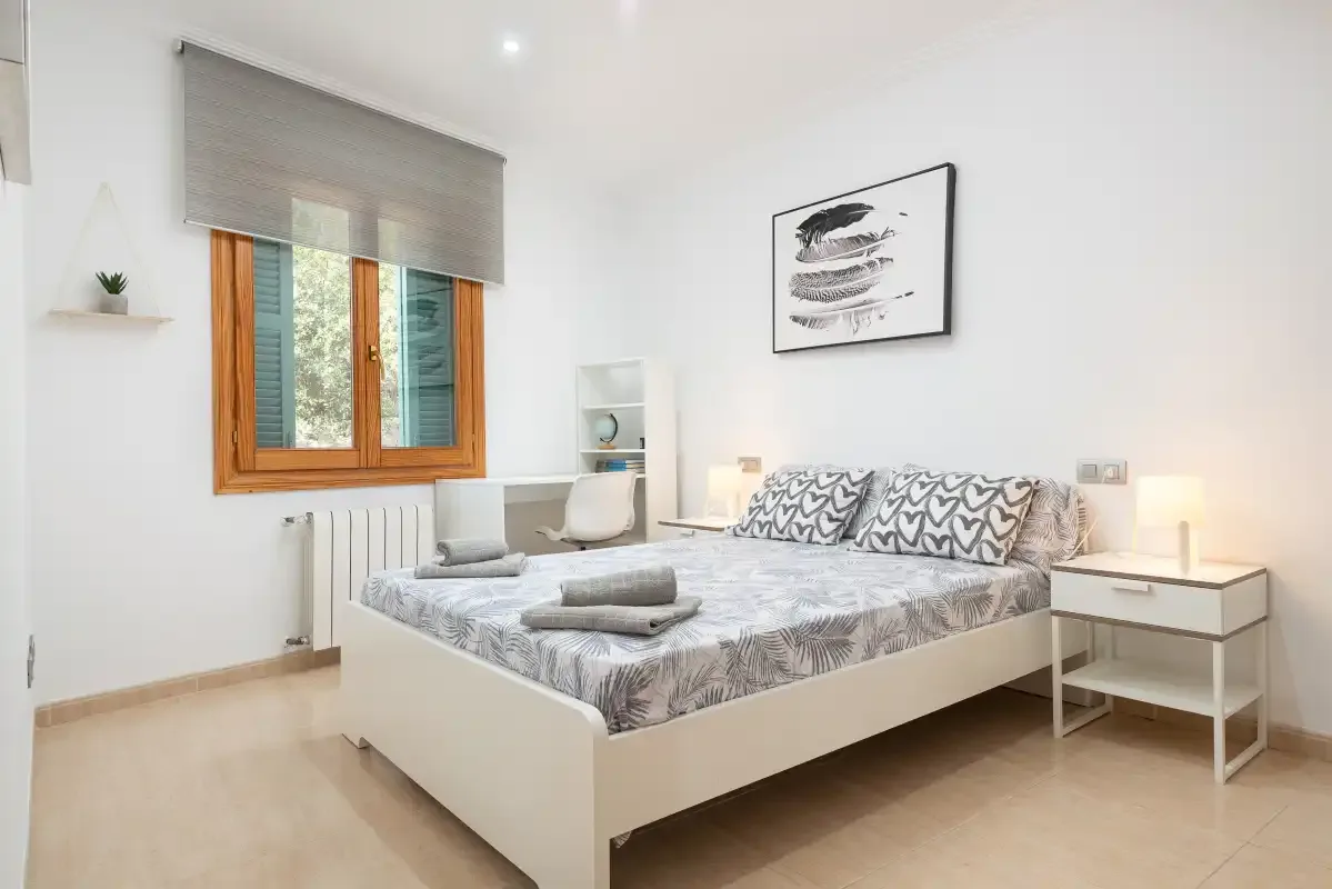 Un dormitorio luminoso con cama doble, mesillas y una ventana.