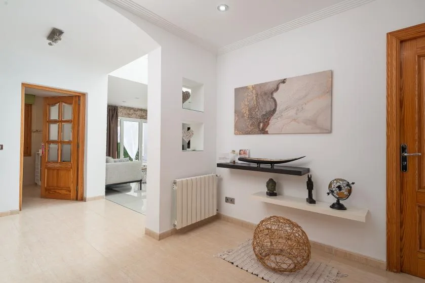 Un pasillo interior luminoso con puertas de madera y una repisa decorativa en la pared.