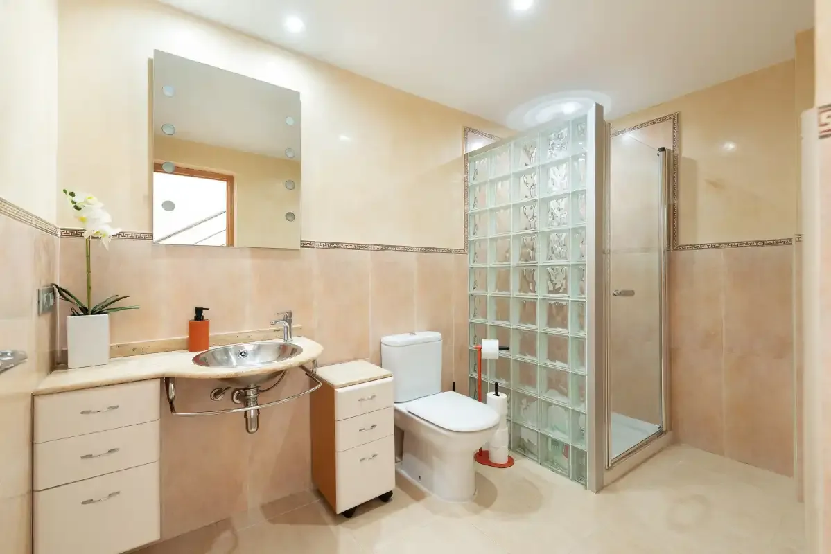 Un baño con lavabo, inodoro y una zona de ducha con bloques de vidrio.