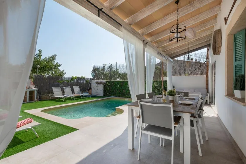 Una zona de comedor exterior cubierta da a una piscina y un jardín.