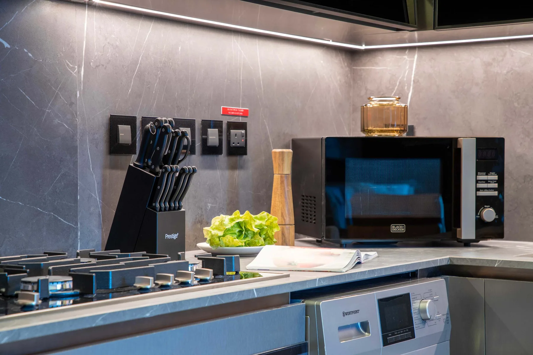 Una encimera de cocina moderna con placa de cocción, microondas y hojas verdes.