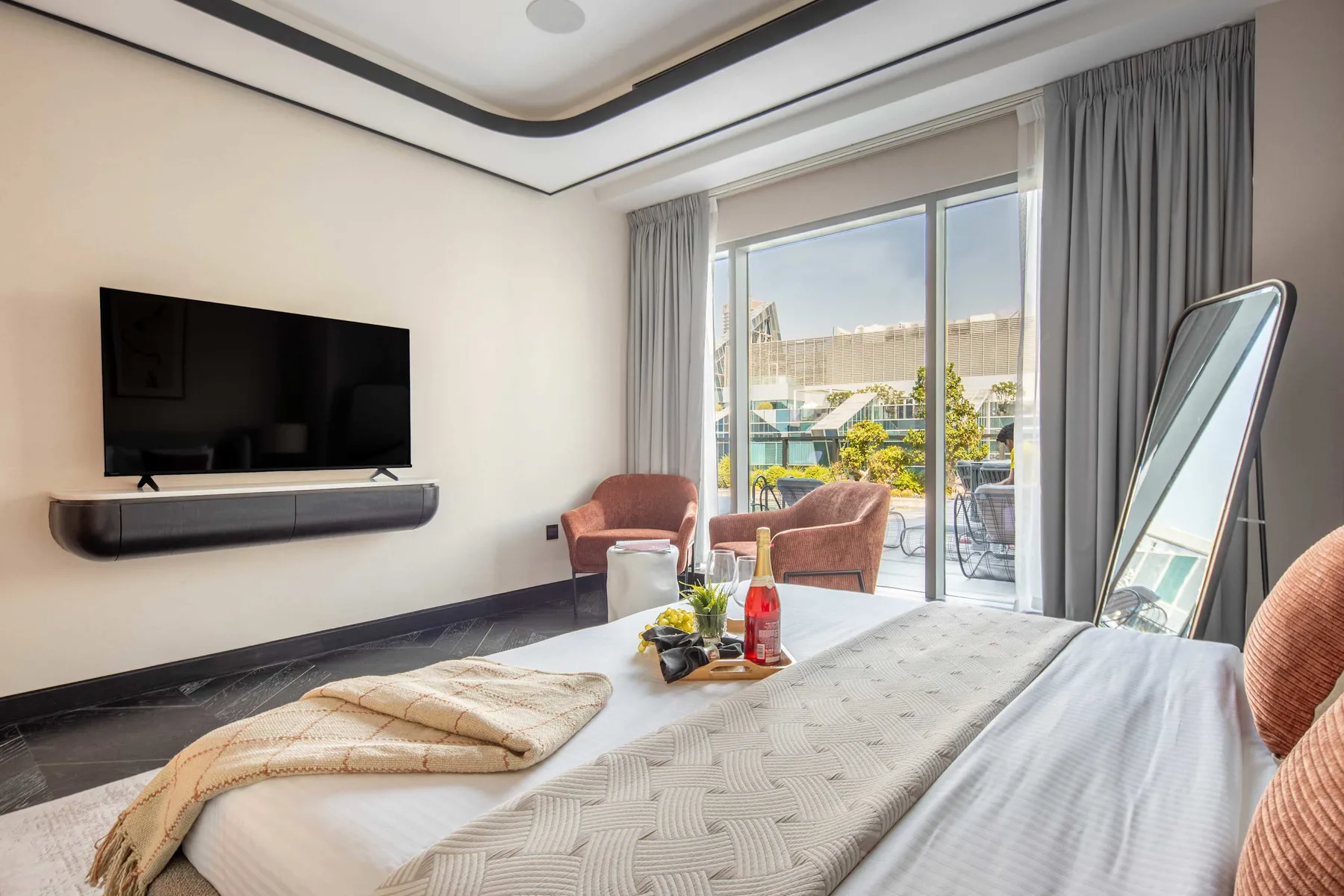 Un dormitorio con una cama, un televisor en la pared y puertas de vidrio que dan a un balcón.