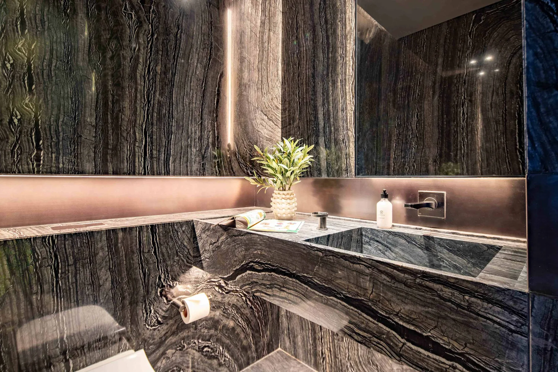 Un baño de piedra oscura con bañera, lavabo y una planta pequeña.