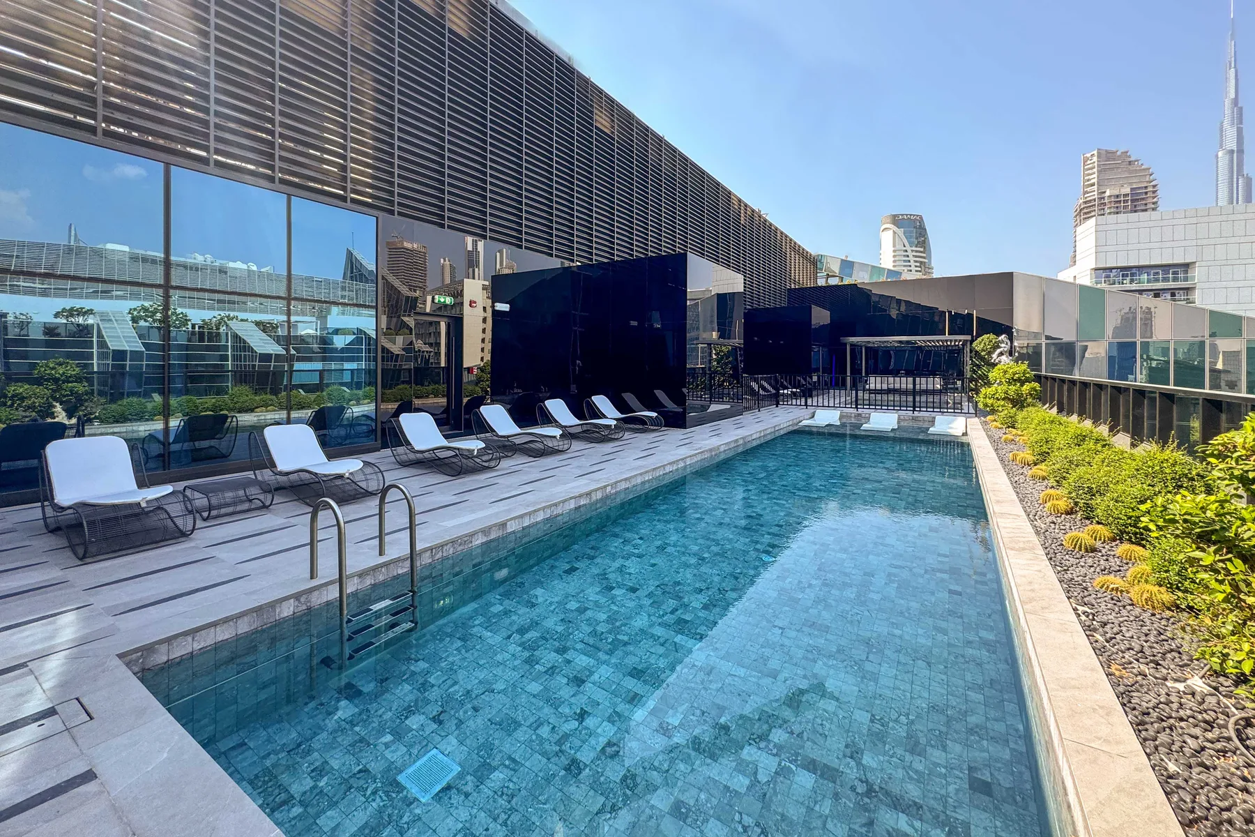 Una piscina en la azotea junto a asientos de descanso y vistas de la ciudad.