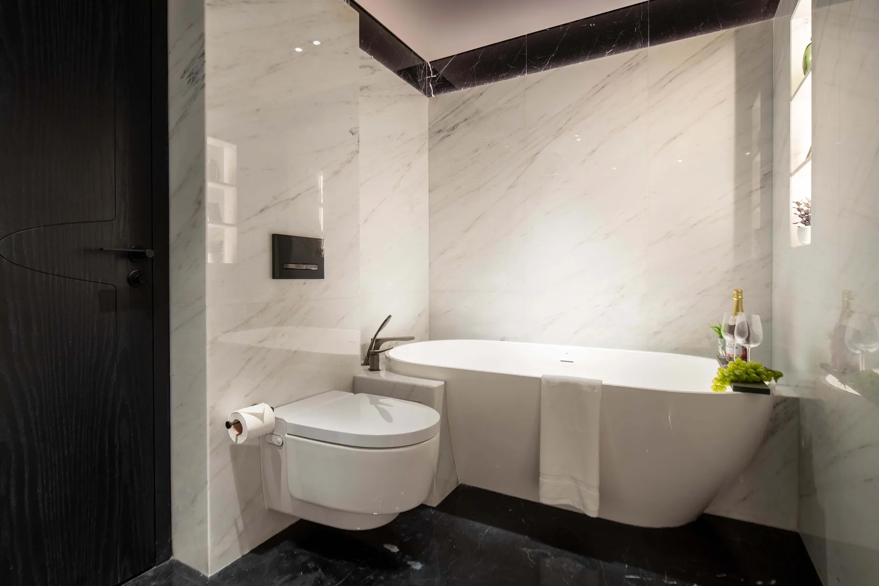 Un baño con bañera, inodoro y paredes claras con vetas.