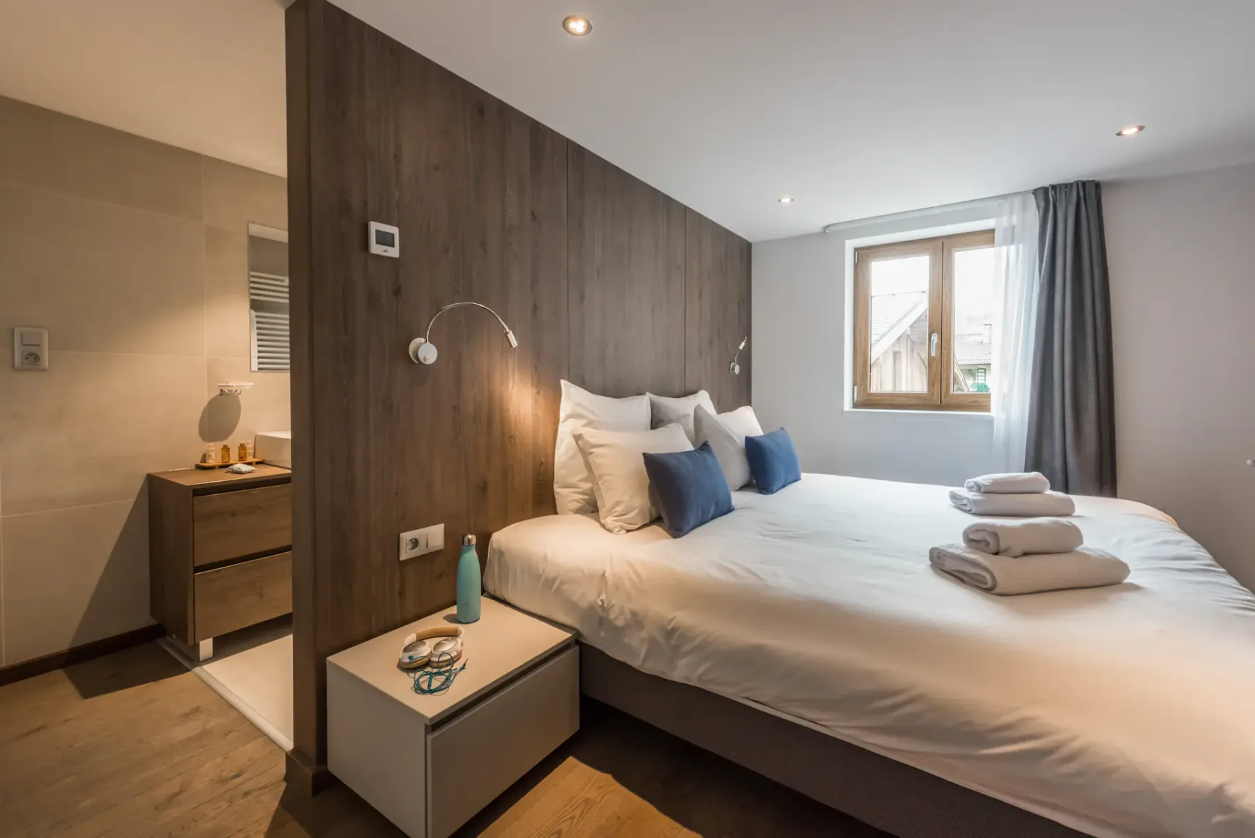 Un dormitorio con una cama bien hecha, una mesita de noche y una ventana.