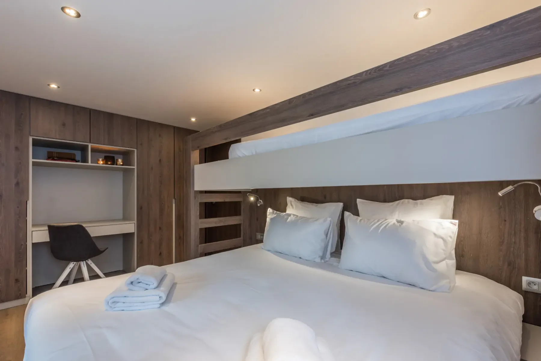 Dormitorio con una cama baja, ropa de cama blanca y paredes revestidas de madera.