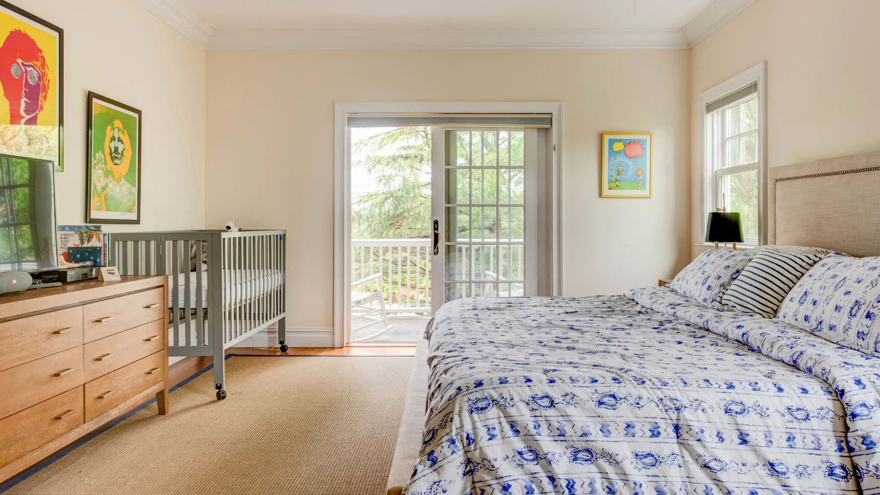 Un dormitorio con una cama grande, una cómoda y una cuna junto a puertas de vidrio.