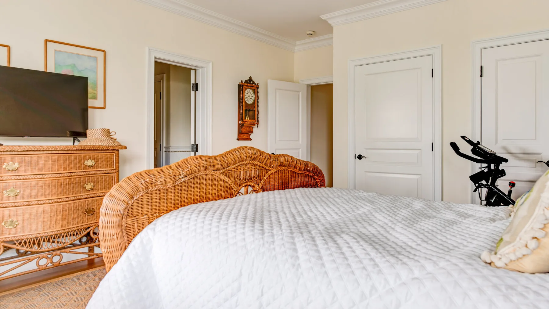 Un dormitorio con una cama grande y asientos de mimbre junto a una cómoda y un televisor.