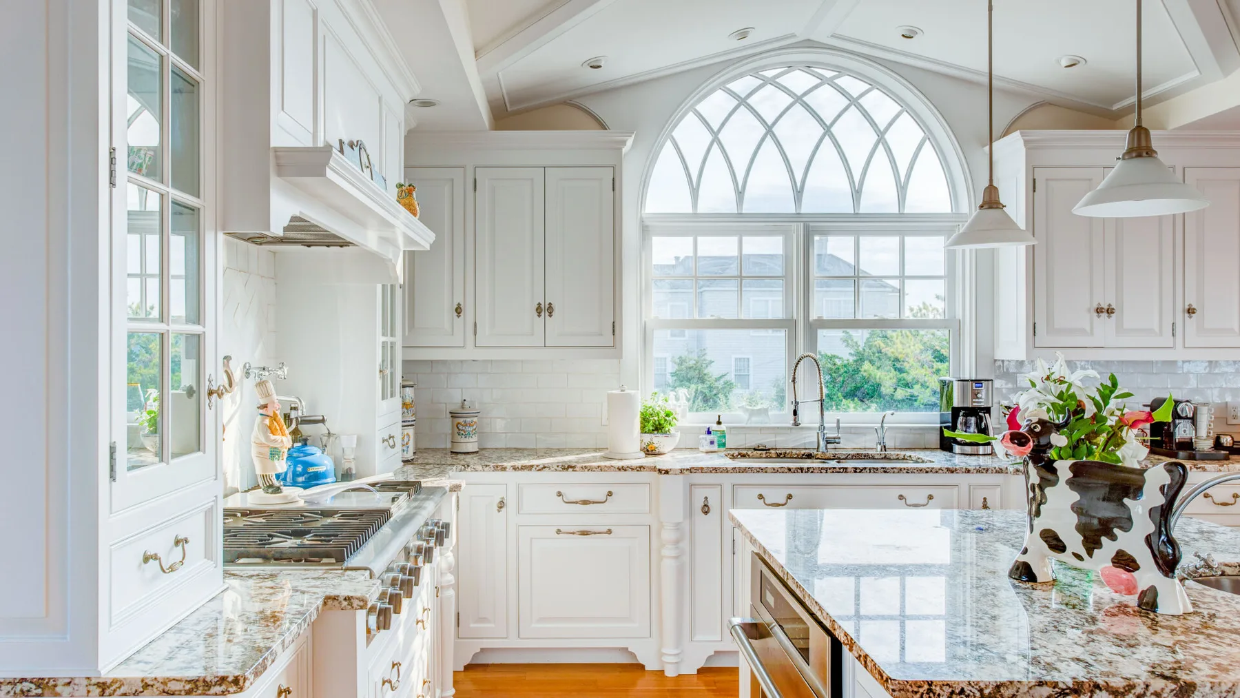 Una cocina blanca y luminosa con una gran ventana arqueada sobre el fregadero.