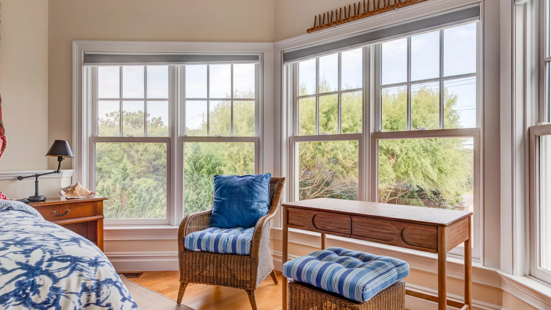 Un dormitorio luminoso con grandes ventanas y una silla de mimbre acolchada.