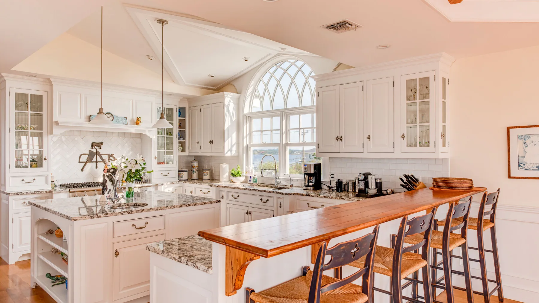 Una cocina luminosa con gabinetes blancos y una larga barra de madera con asientos.