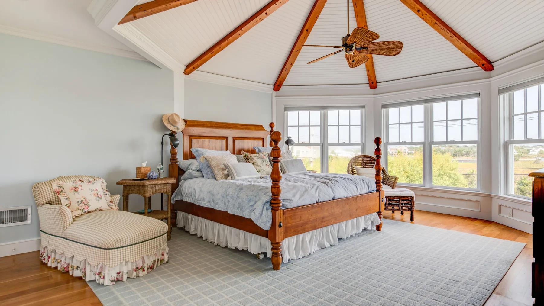 Un dormitorio con una cama de madera bajo un techo alto con vigas y amplias ventanas.