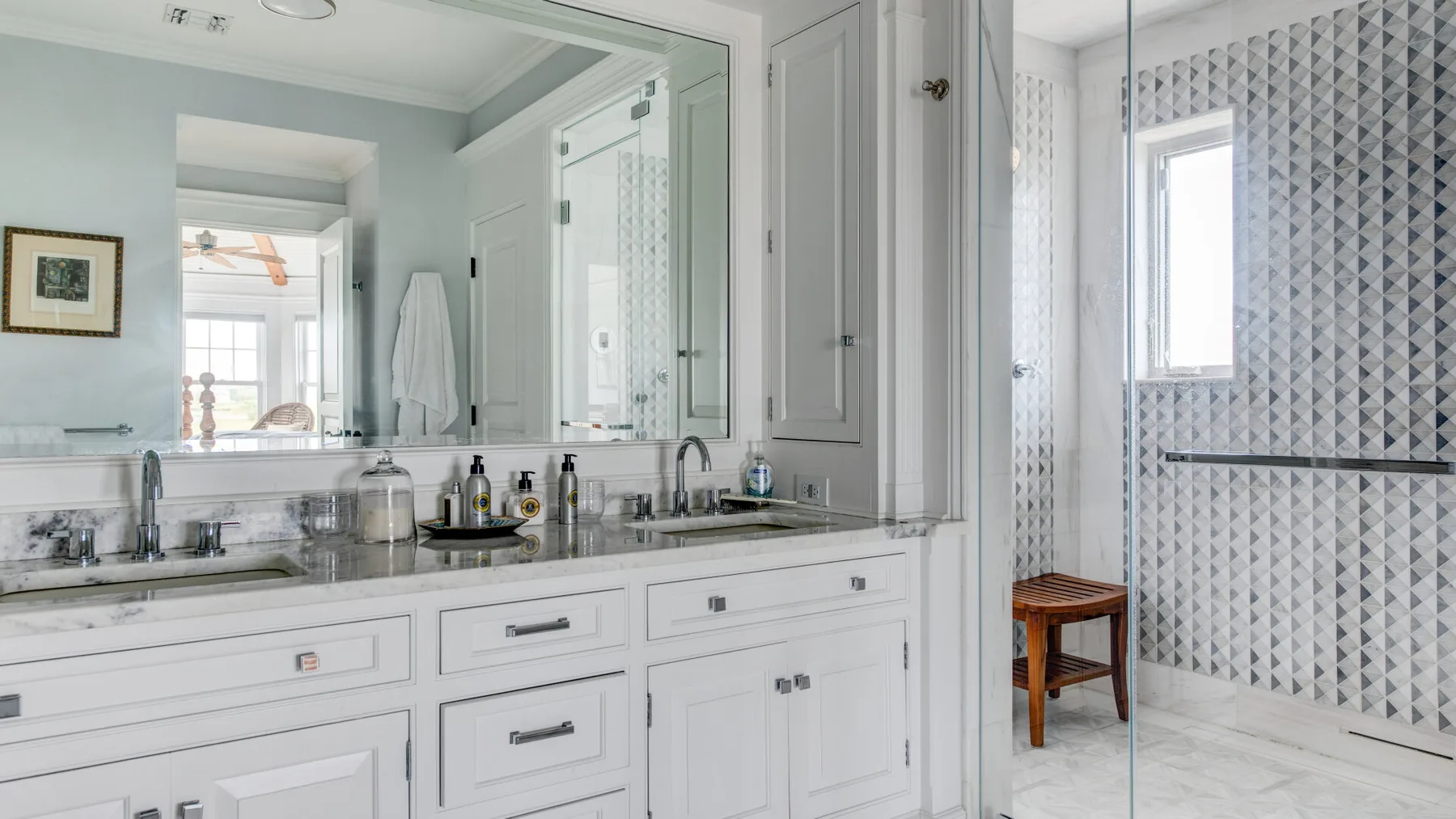 Un tocador de baño luminoso con un espejo amplio junto a una ducha con azulejos.