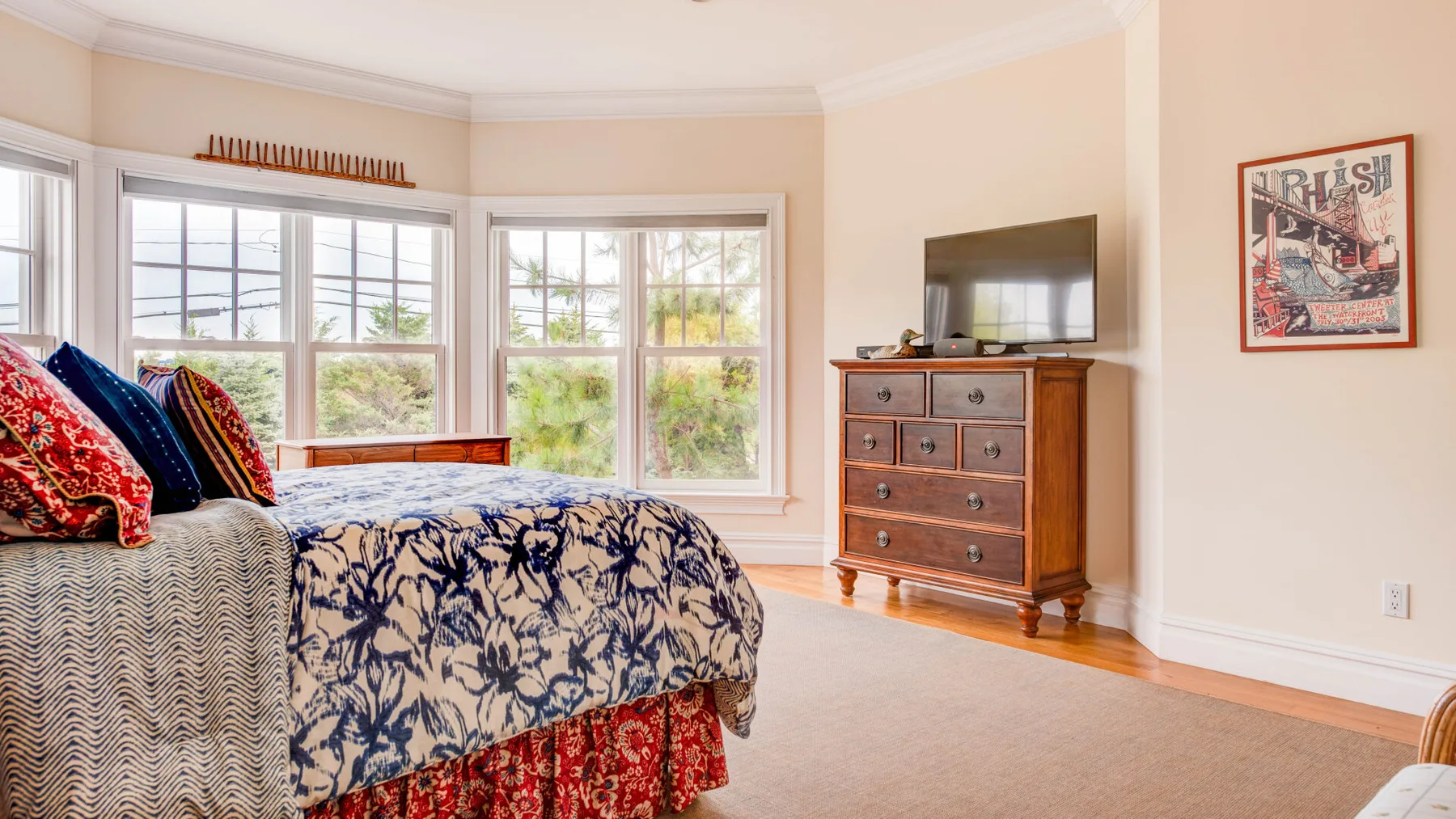 Un dormitorio con una cama estampada, una cómoda de madera y ventanas.