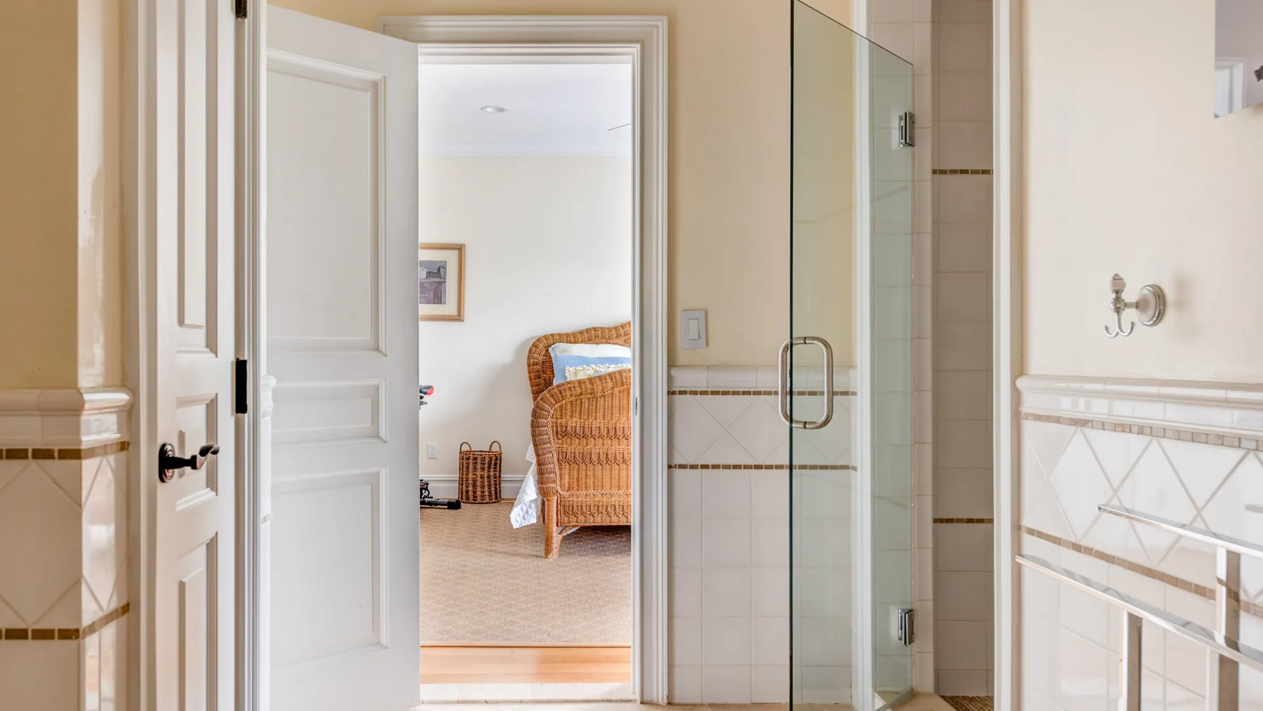 Un baño con azulejos, una ducha de cristal y una puerta abierta a una habitación luminosa.