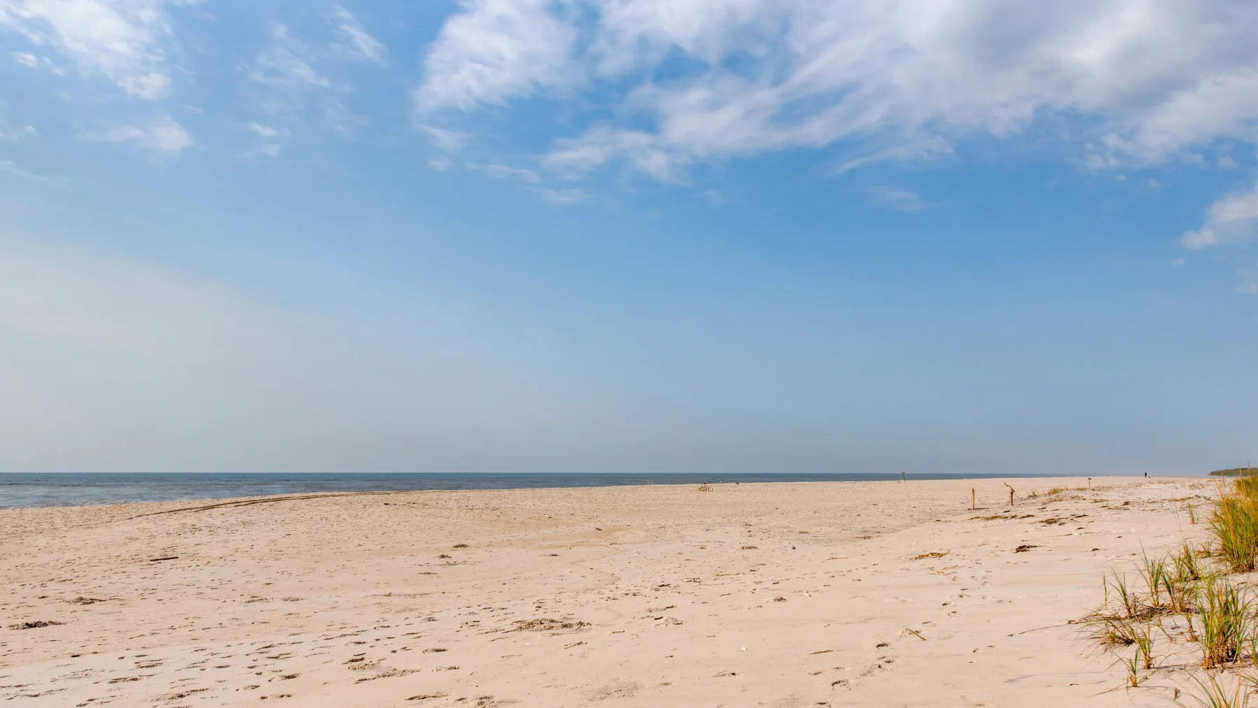 Una playa de arena se extiende junto al agua bajo un cielo parcialmente nublado.