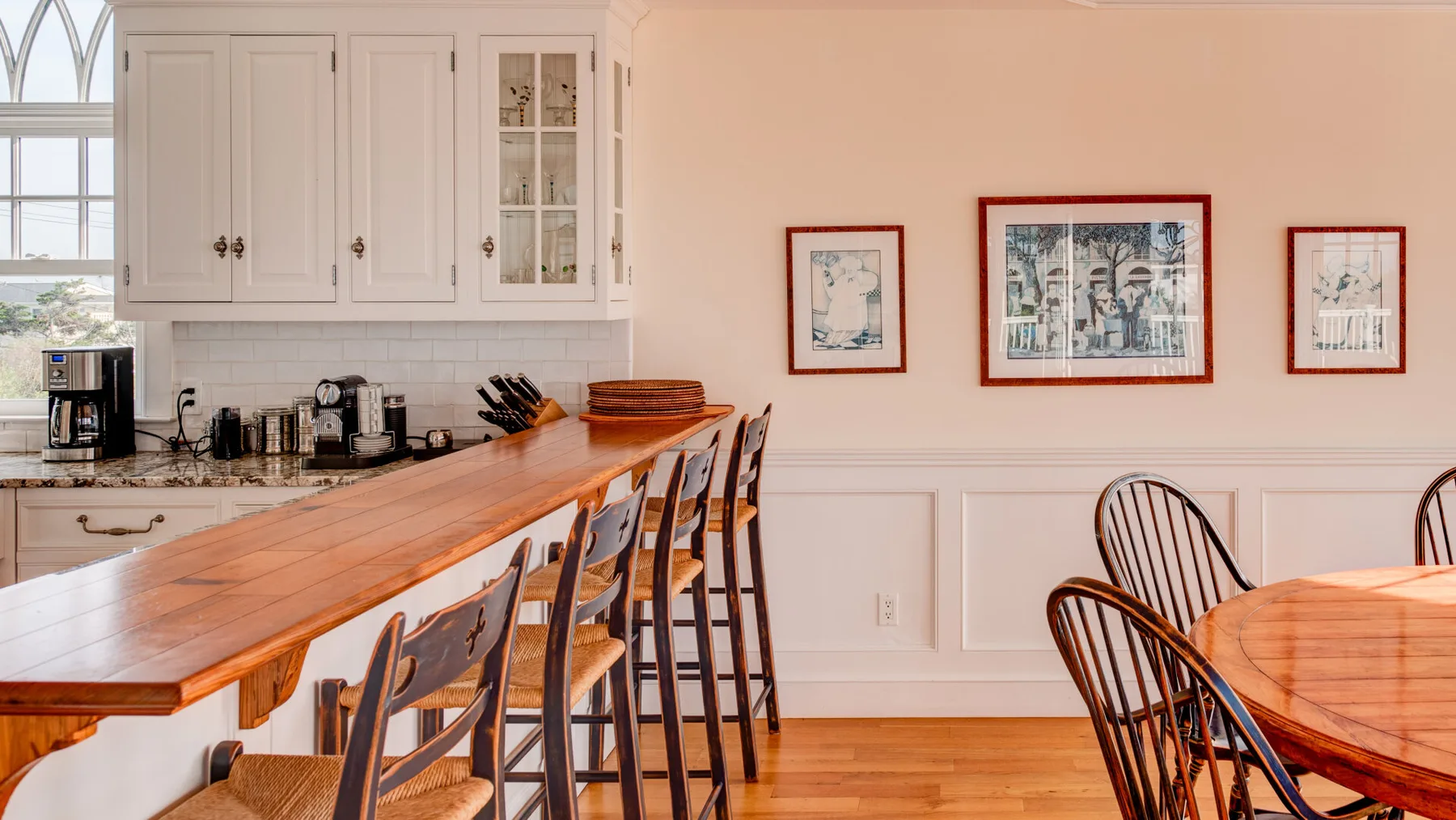 Una cocina y comedor luminosos con una larga barra de madera y cuadros en la pared.