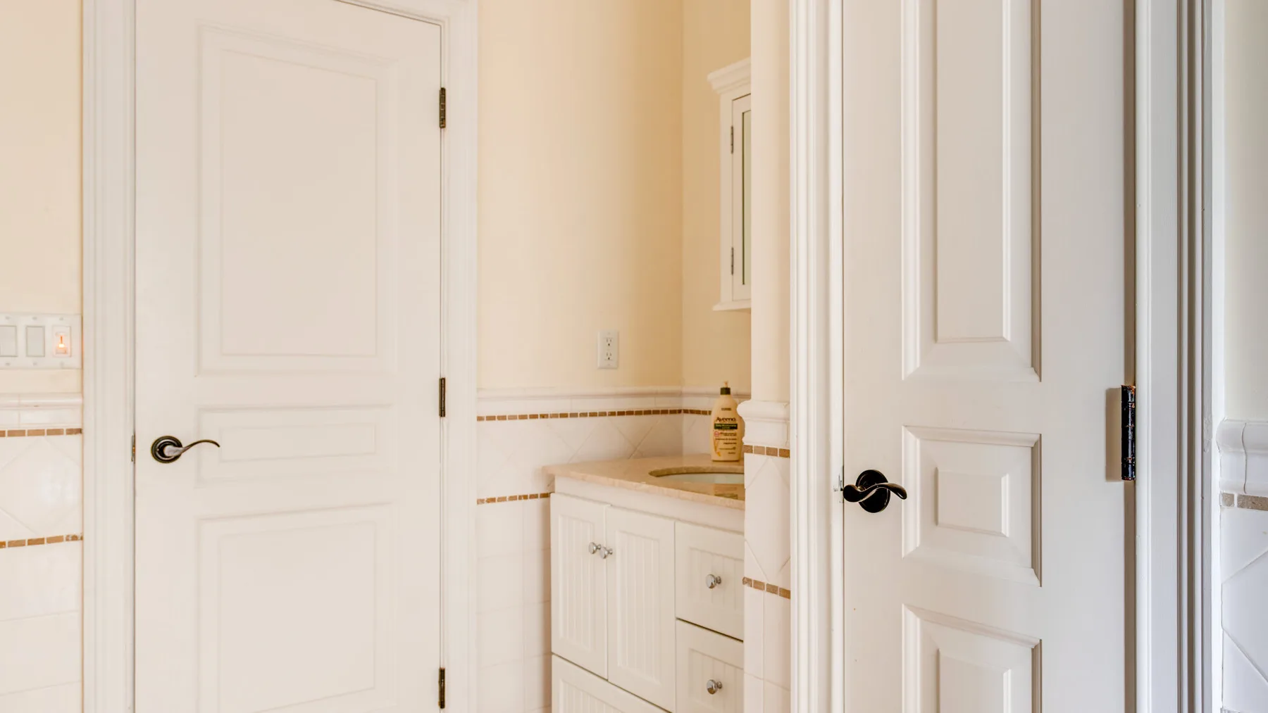 Un baño luminoso con gabinetes blancos y puertas con paneles.