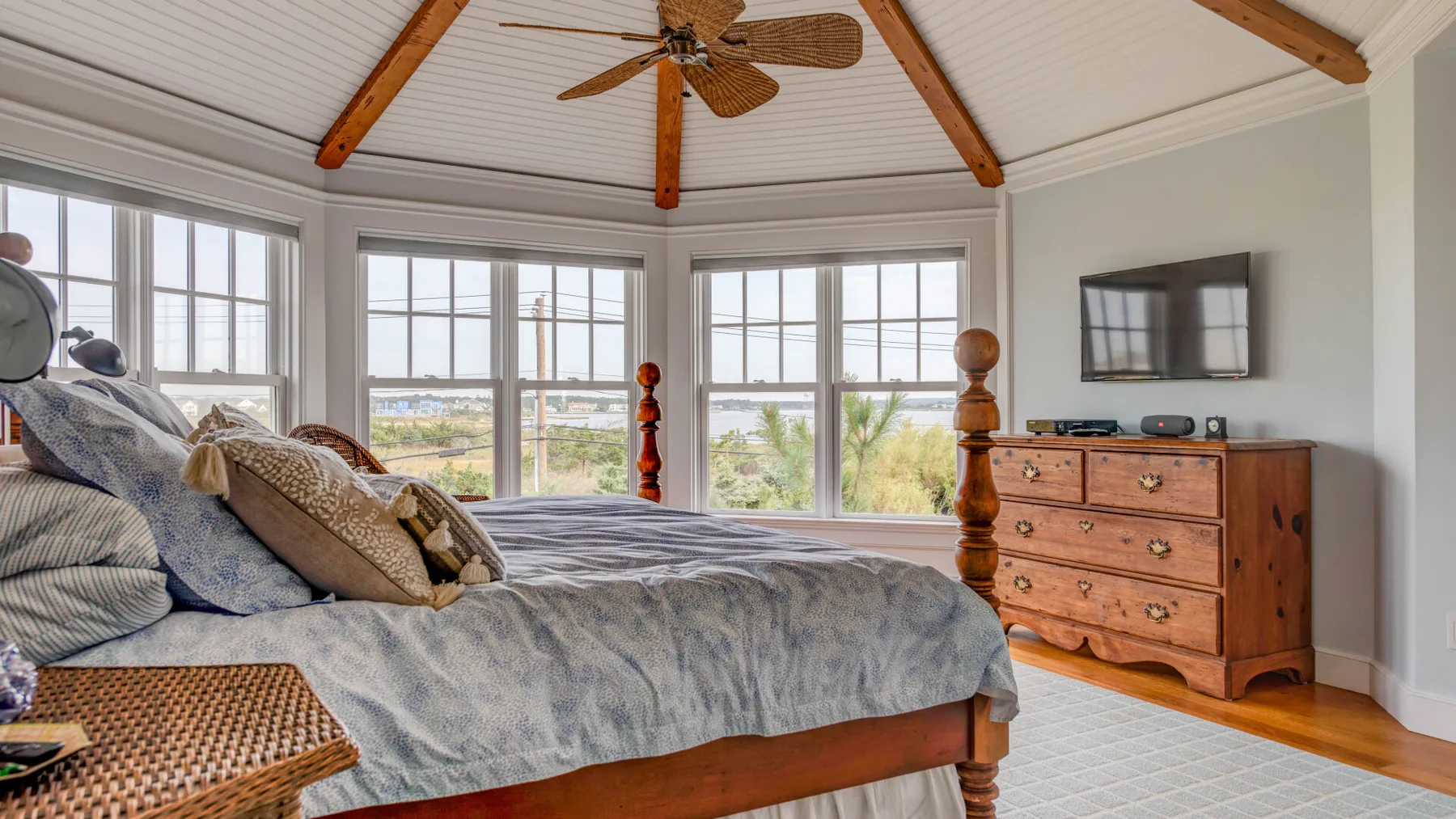 Un dormitorio luminoso con una cama grande, amplias ventanas y una cómoda de madera.