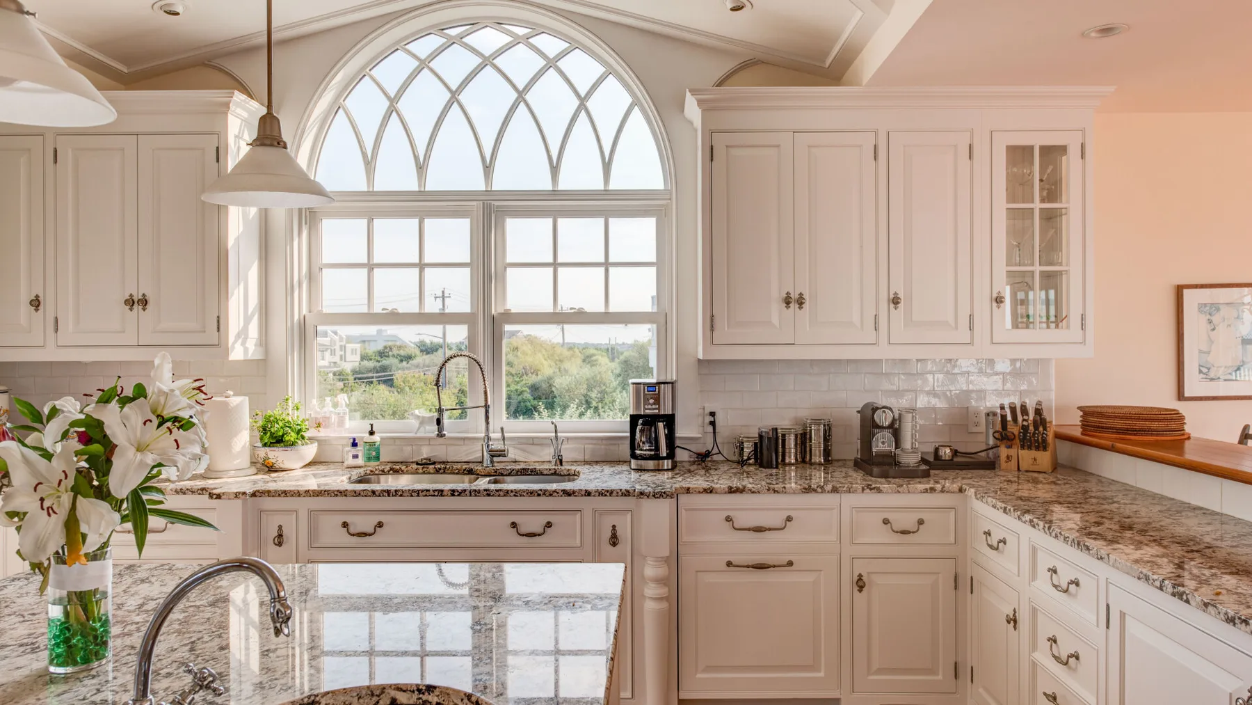 Una cocina luminosa con gabinetes claros, encimeras de piedra y una gran ventana arqueada.