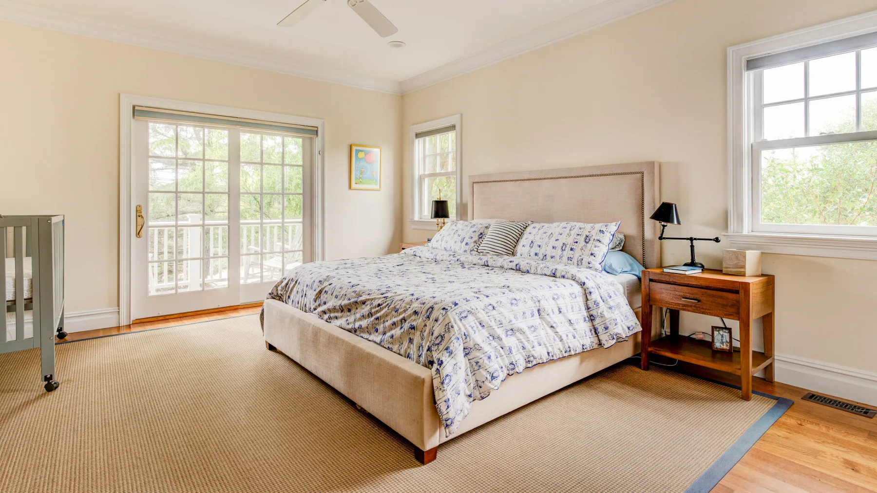 Un dormitorio luminoso con una cama junto a grandes ventanas y una mesita de madera.