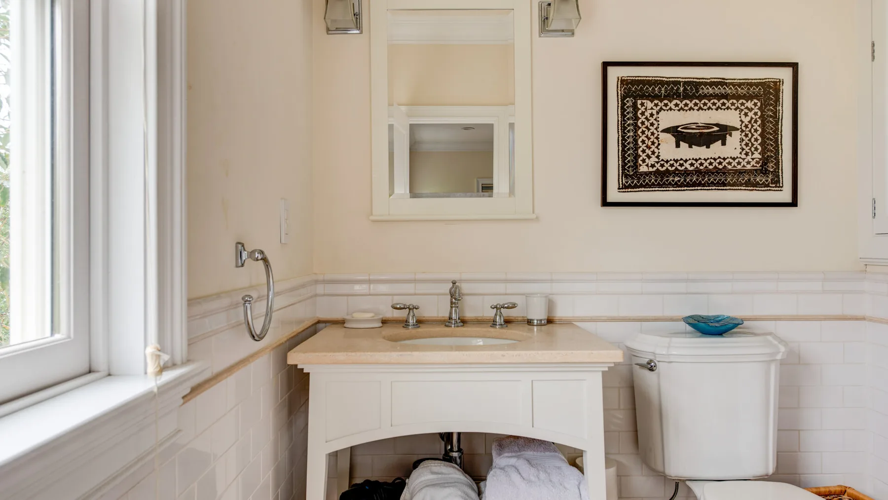 Un lavabo con espejo está junto a una ventana y un inodoro.