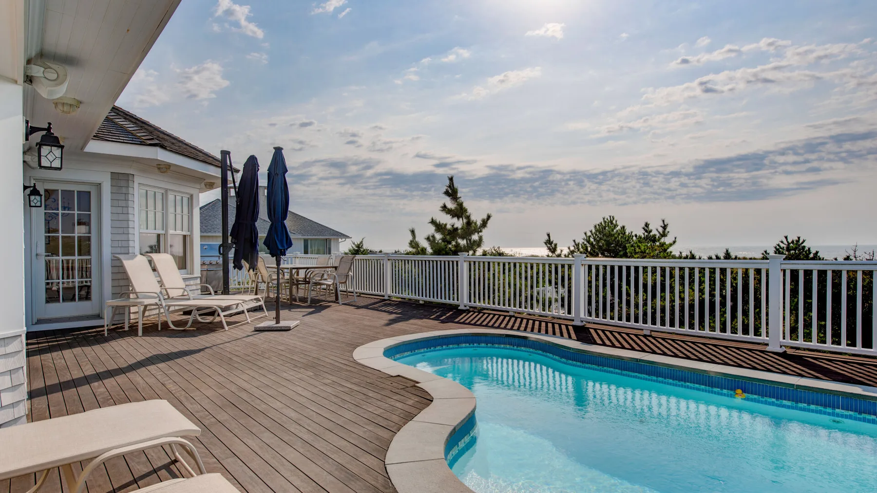 Una piscina está junto a una terraza de madera con asientos y una barandilla.
