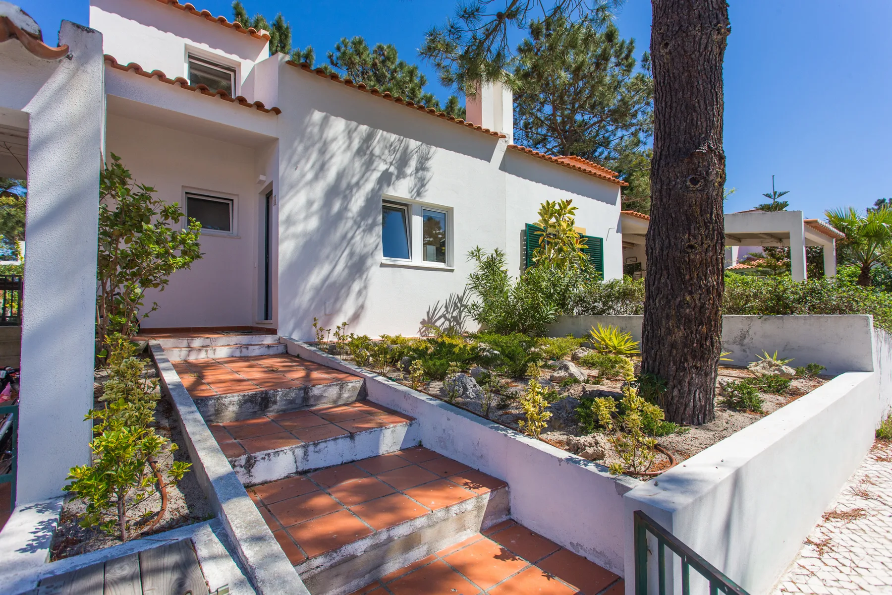 Exterior de una casa blanca con escalones de baldosas hacia la entrada y un jardín.
