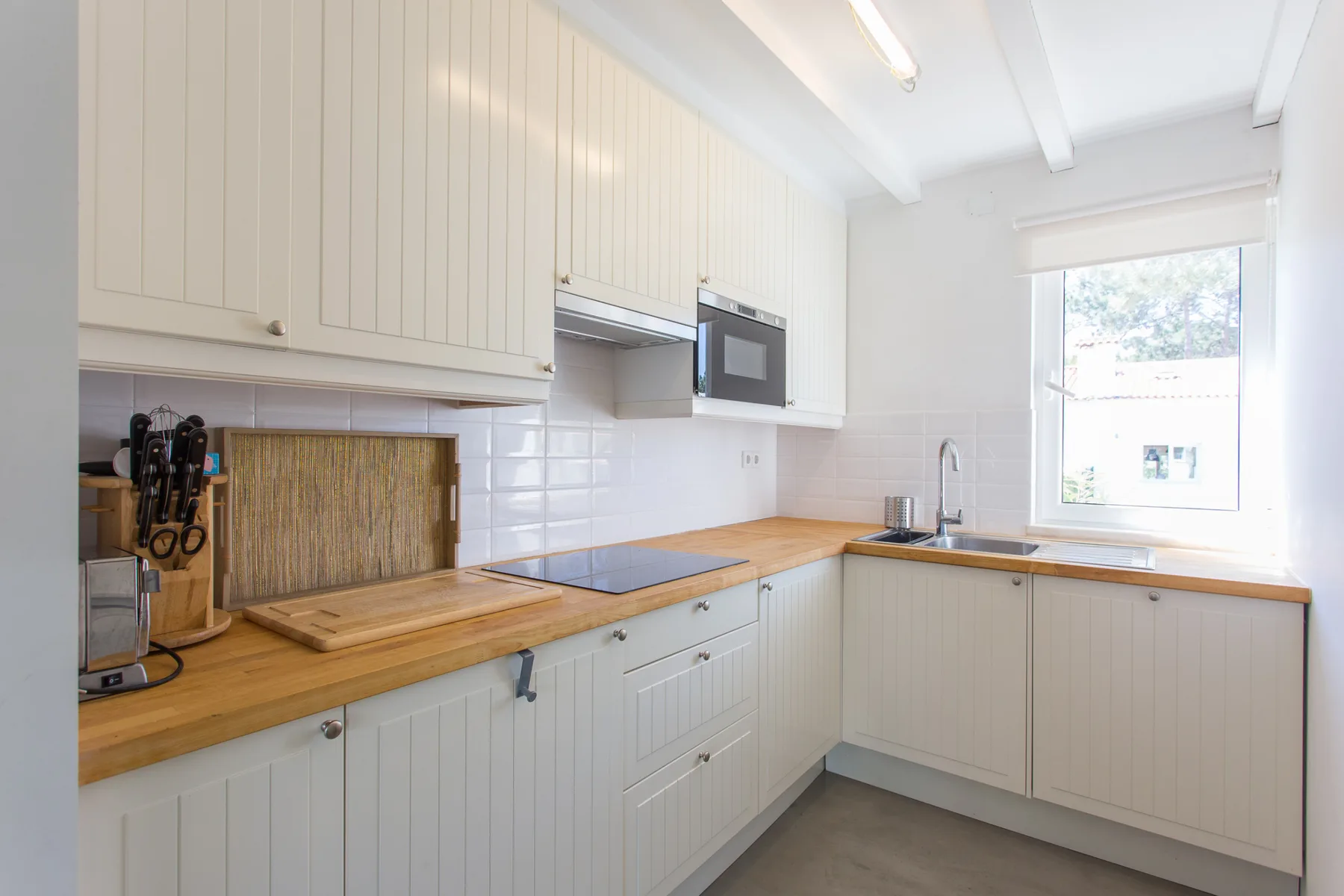 Una cocina luminosa con armarios blancos, encimeras de madera y una ventana.