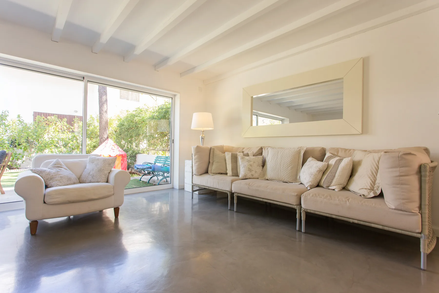 Sala de estar luminosa con asientos beige y grandes ventanas con vistas a la vegetación.