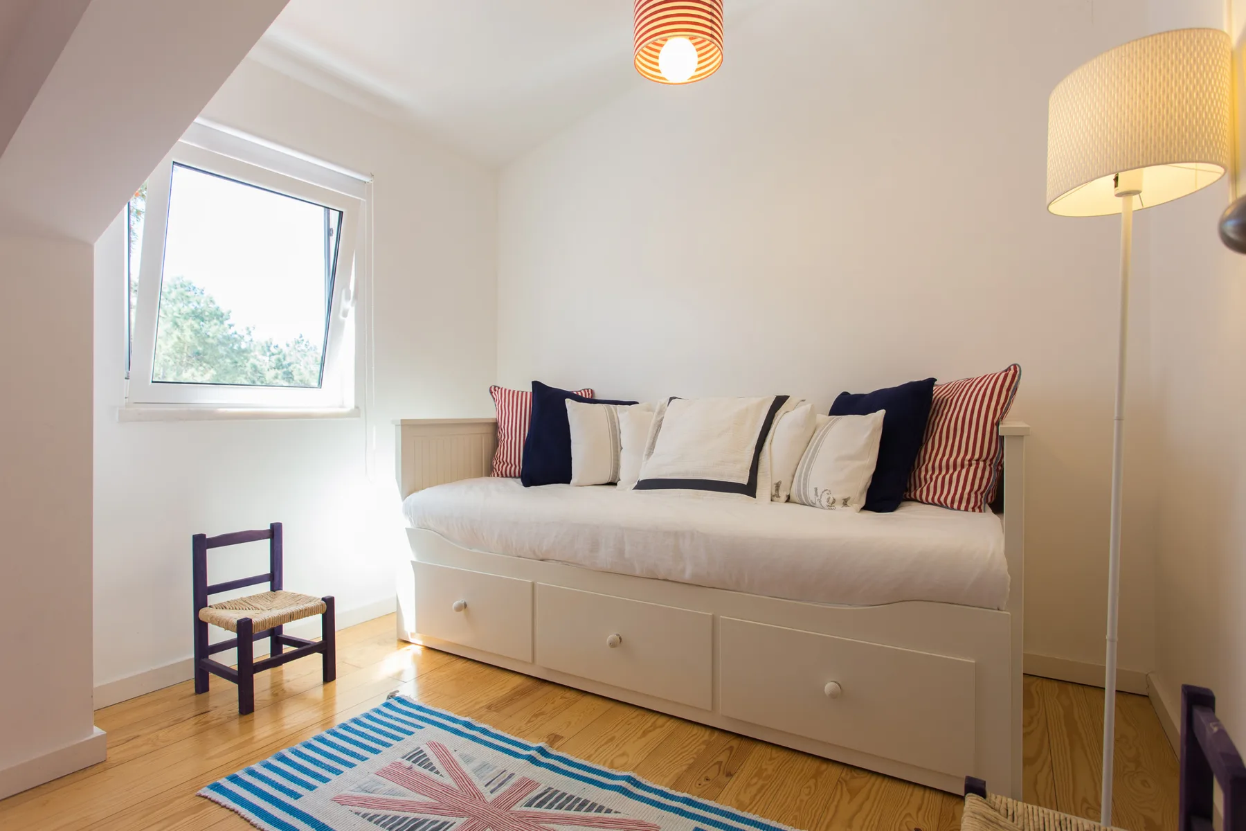 Un dormitorio luminoso con una cama nido, cojines estampados y una alfombra colorida.